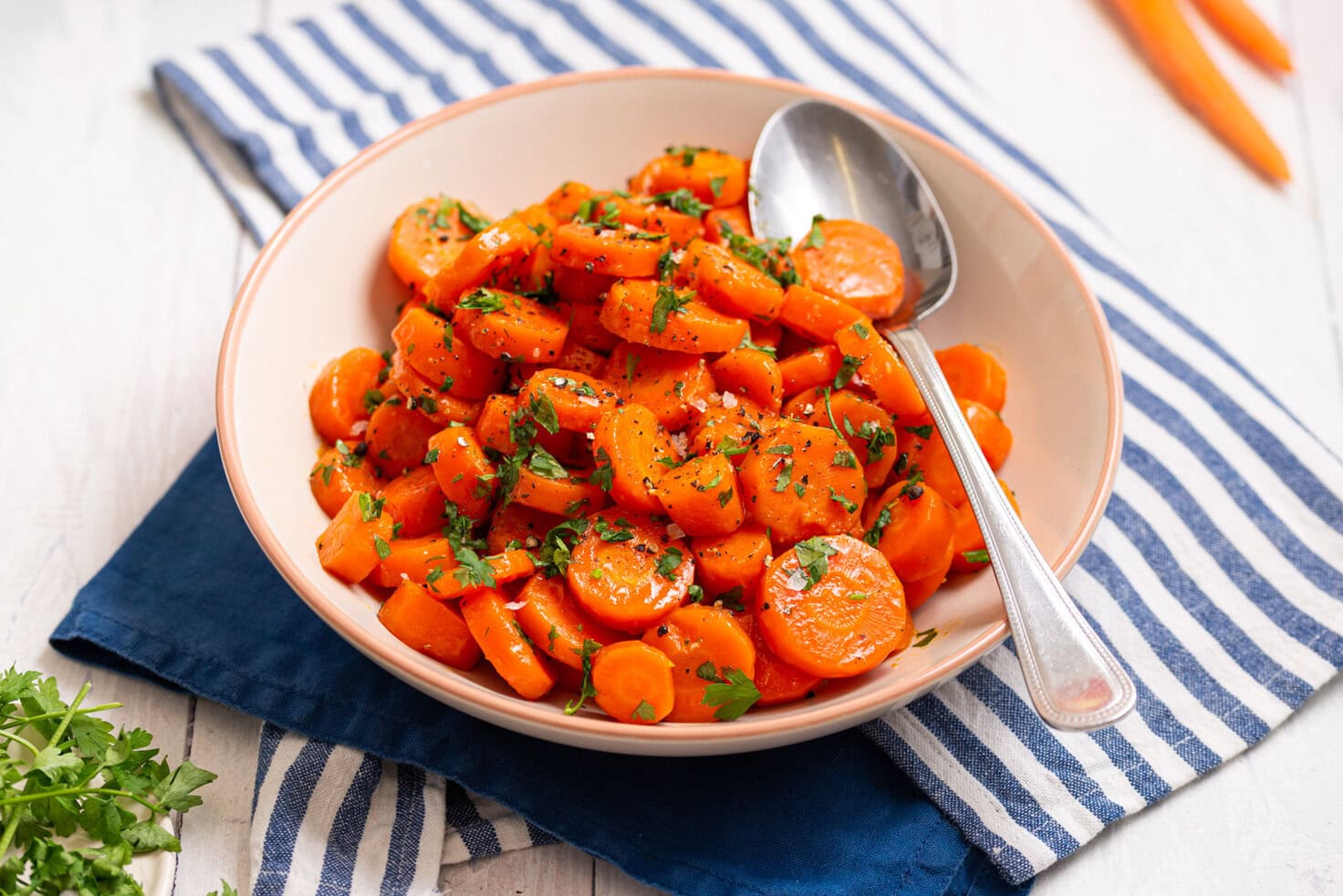 Brown sugar glazed carrots served in a bowl with a spoon and fresh parsley.