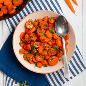 Brown sugar glazed carrots with a glossy glaze, black pepper, and fresh parsley in a bowl.