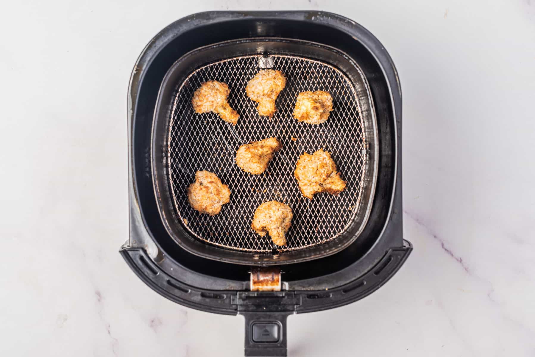 An image of cauliflower florets in an air fryer, half cooked