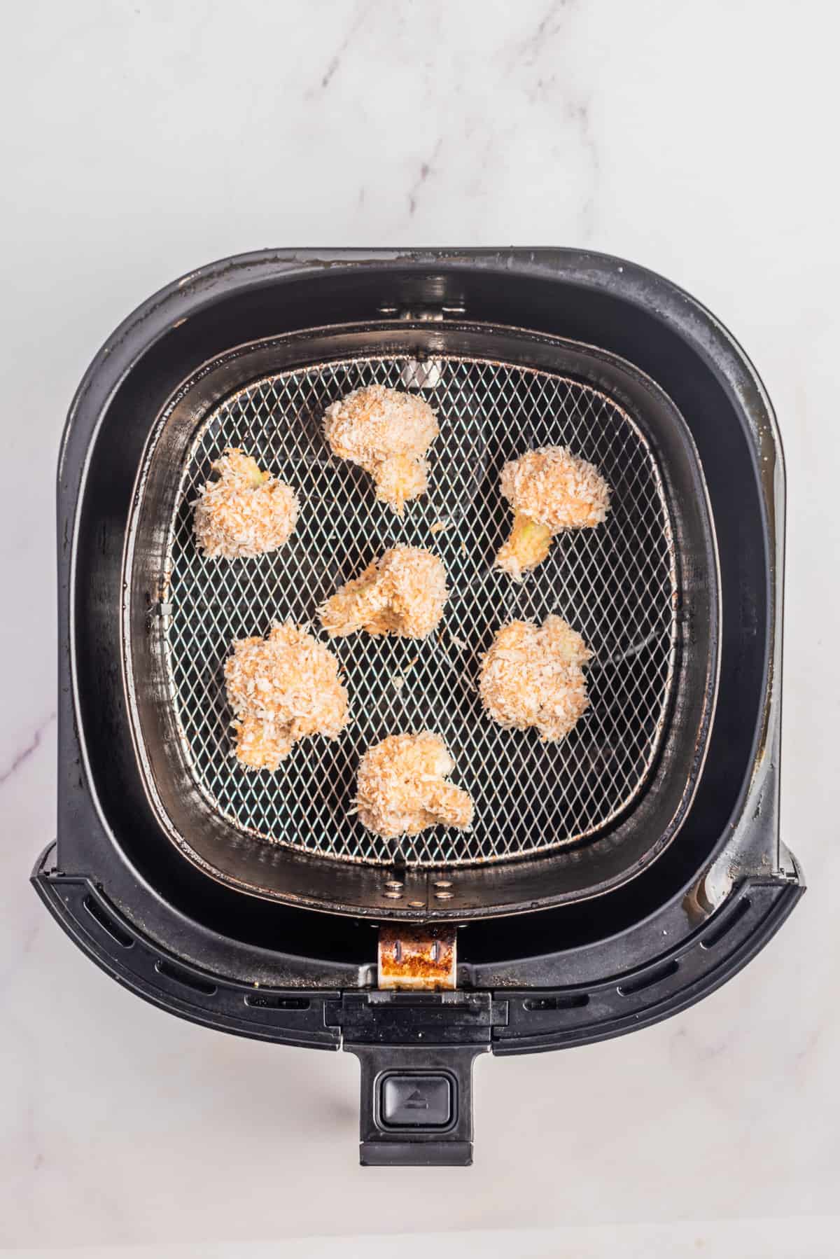 An image of cauliflower florets in an air fryer before cooking