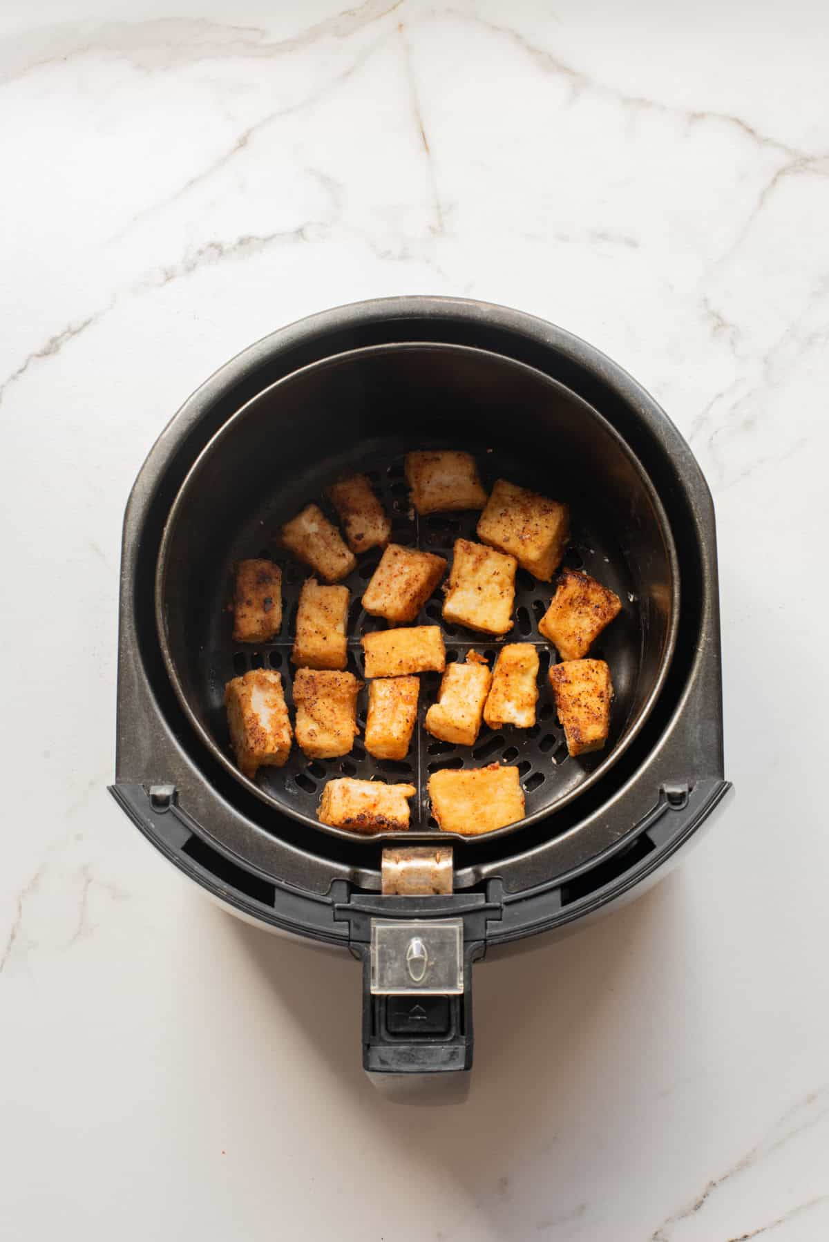 An overhead image of crispy cooked tofu in an air fryer.