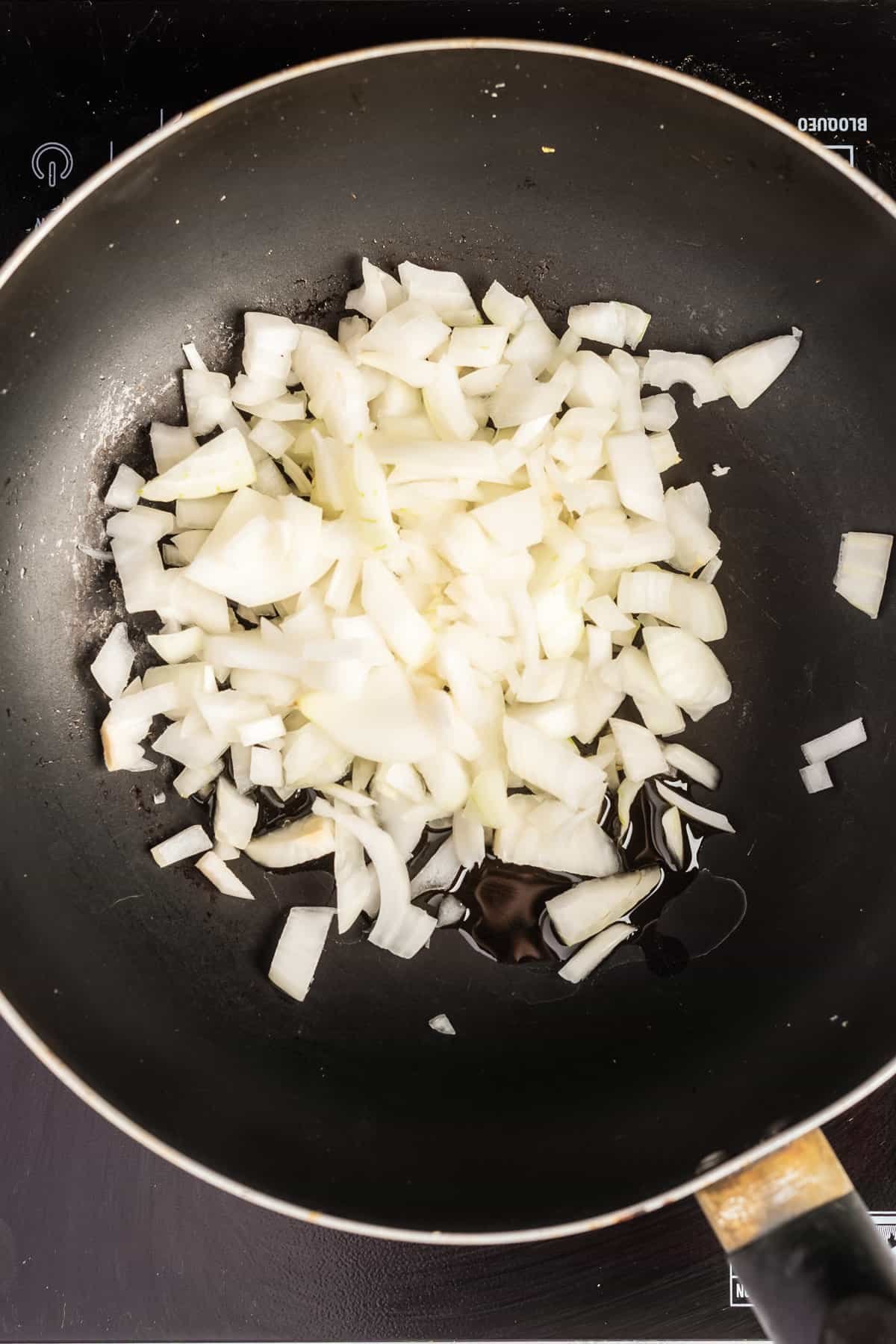 Overhead view of a pan with avocado oil and chopped onions.