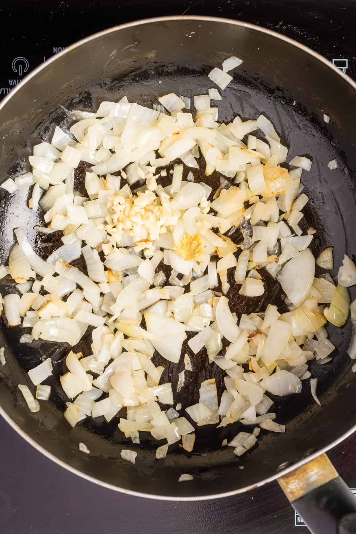 Overhead view of chopped onions sautéed in a pan with garlic and ginger. 