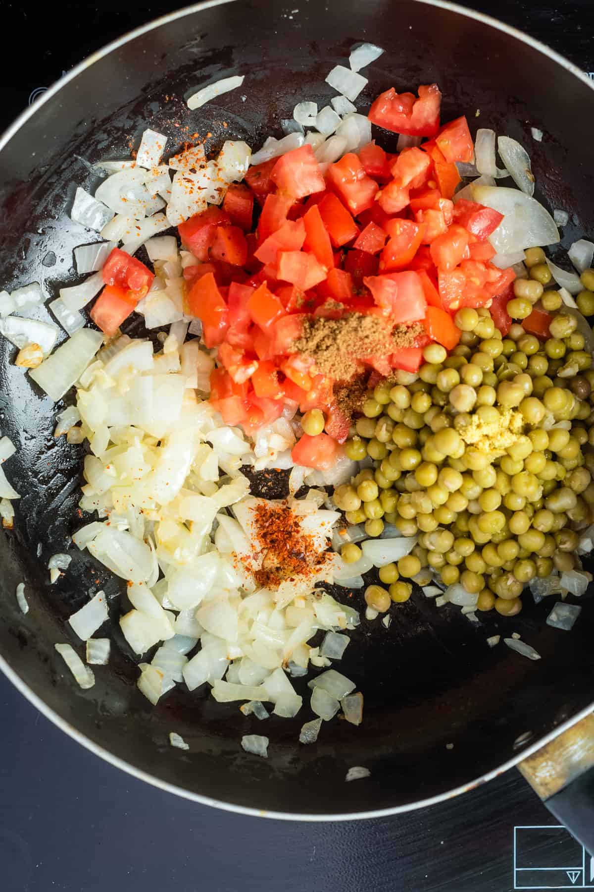 Overhead view of sauteed chopped onions, garlic, and ginger added with tomatoes, peas, turmeric, garam masala, and red chili powder.