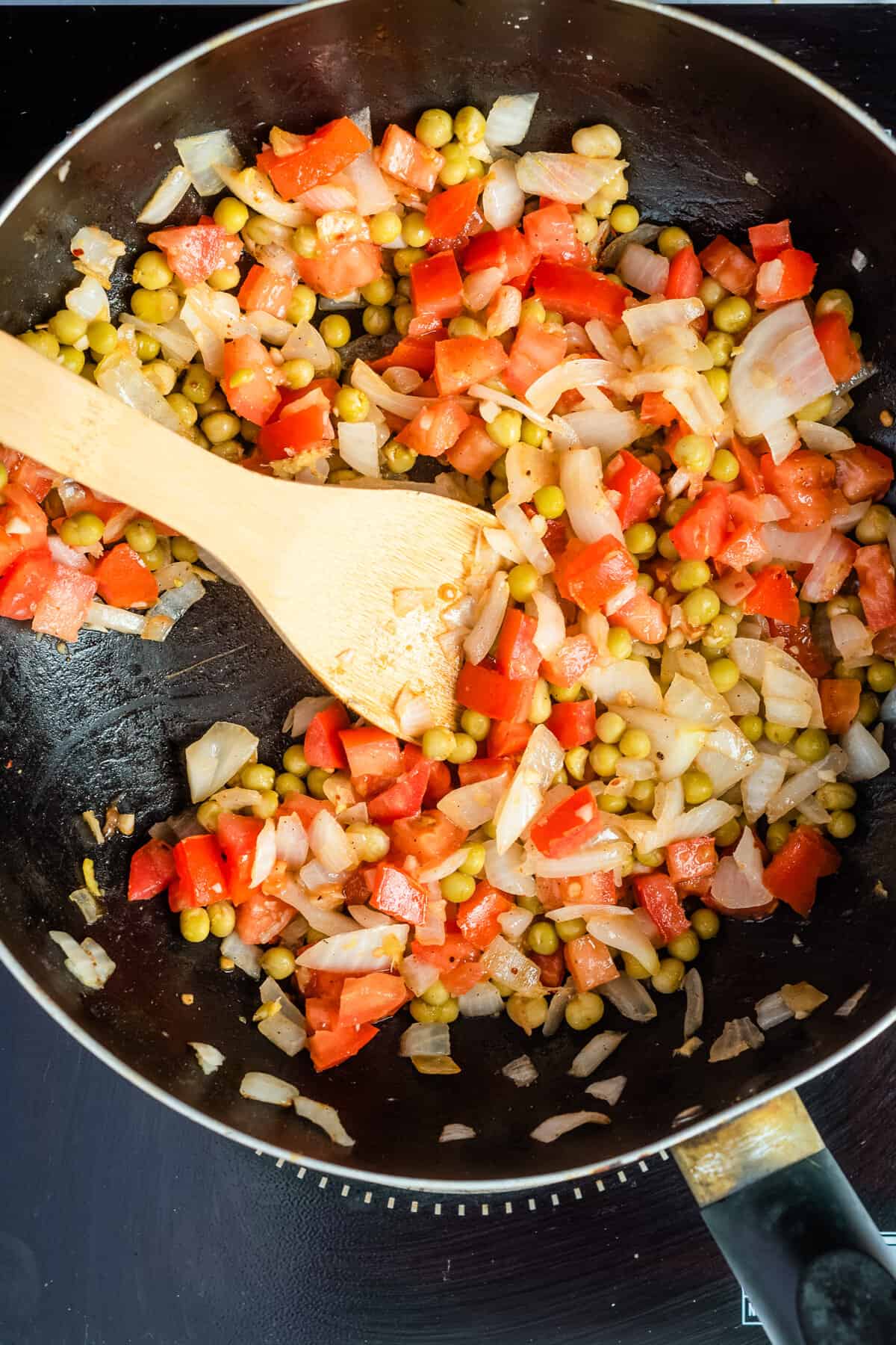 Overhead view of mixed chopped onions, garlic, ginger, tomatoes, peas, turmeric, garam masala, and red chili powder.