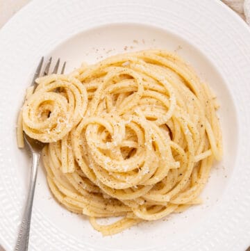 Close up of cacio e pepe in a white bowl with a fork on the side.