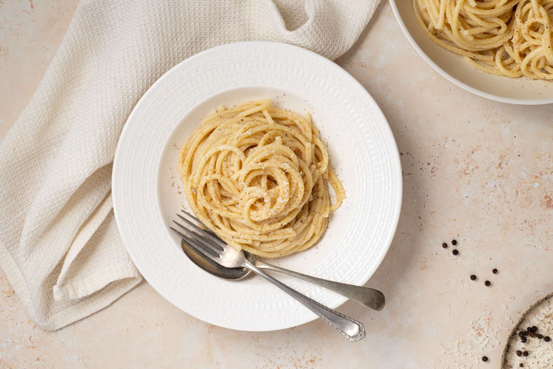 Close up of cacio e pepe in white bowl with fork and spoon.