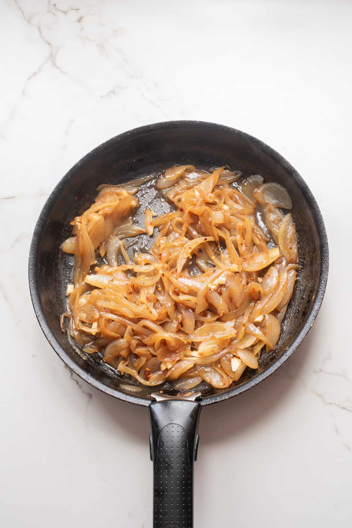 An overhead image of adding garlic and red chili flakes in a skillet.