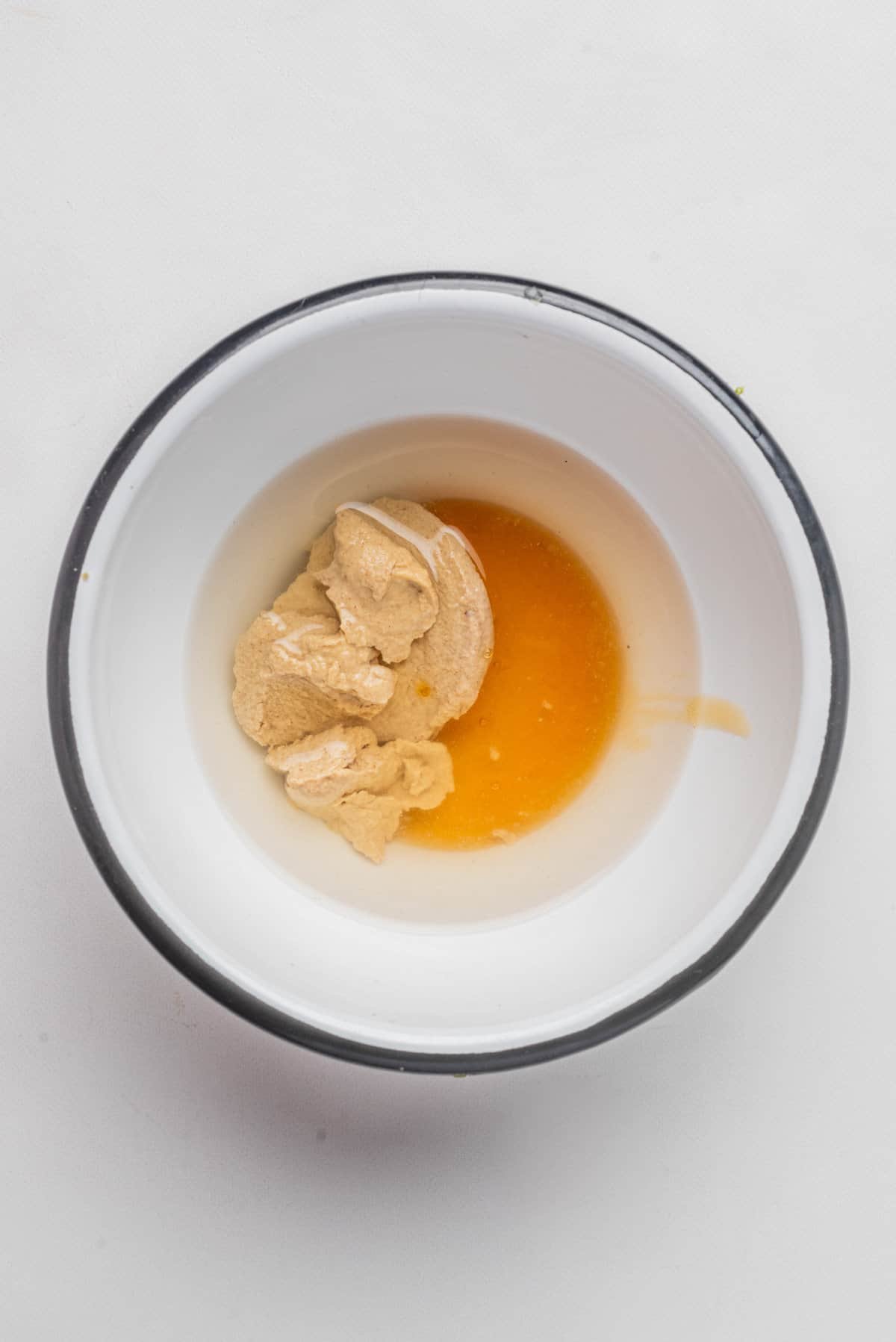 An overhead image of a mixing bowl with champagne vinegar, dijon mustard, and maple syrup, before mixing them all together.