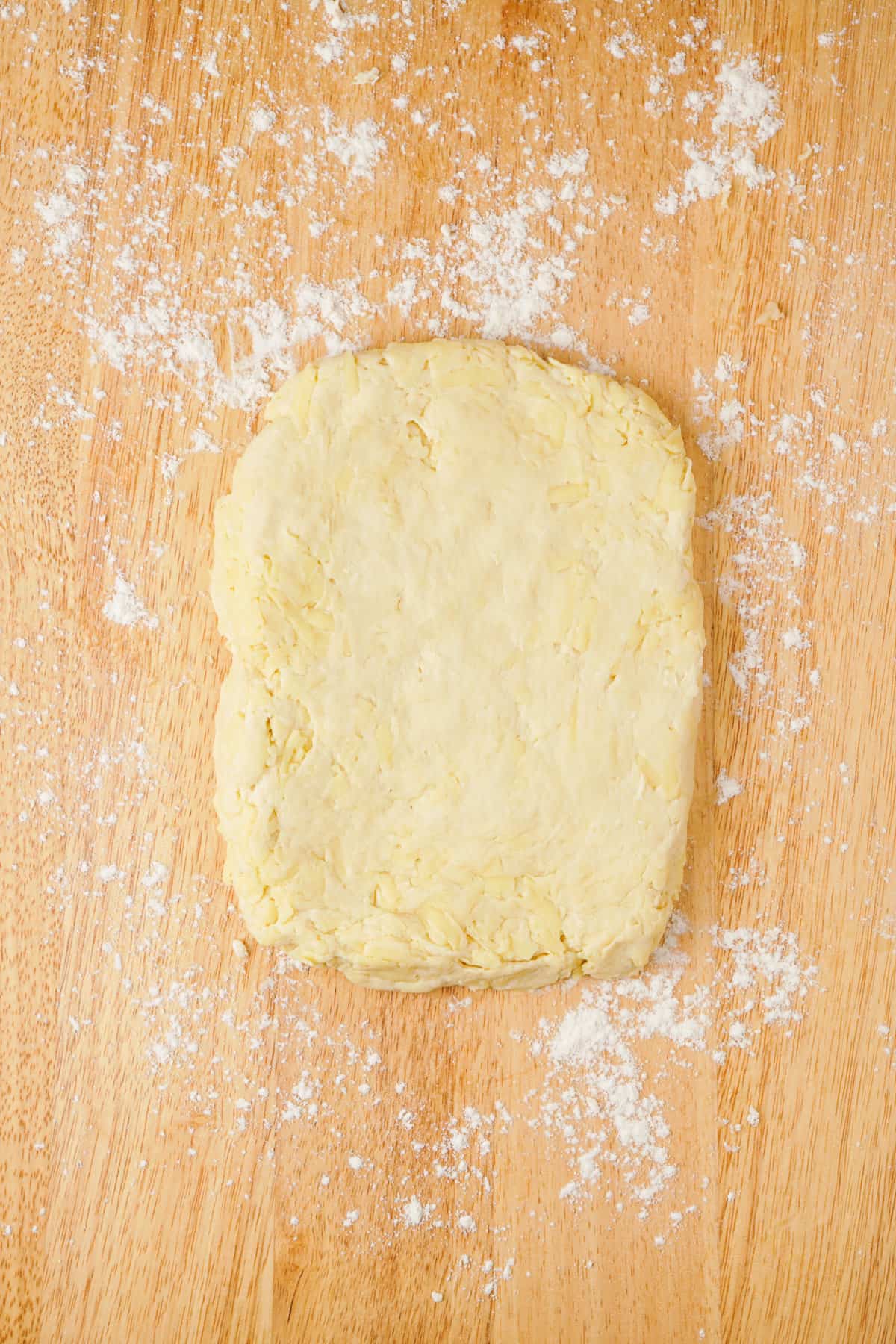 Overhead view showing dough flattened on a wooden cutting board.