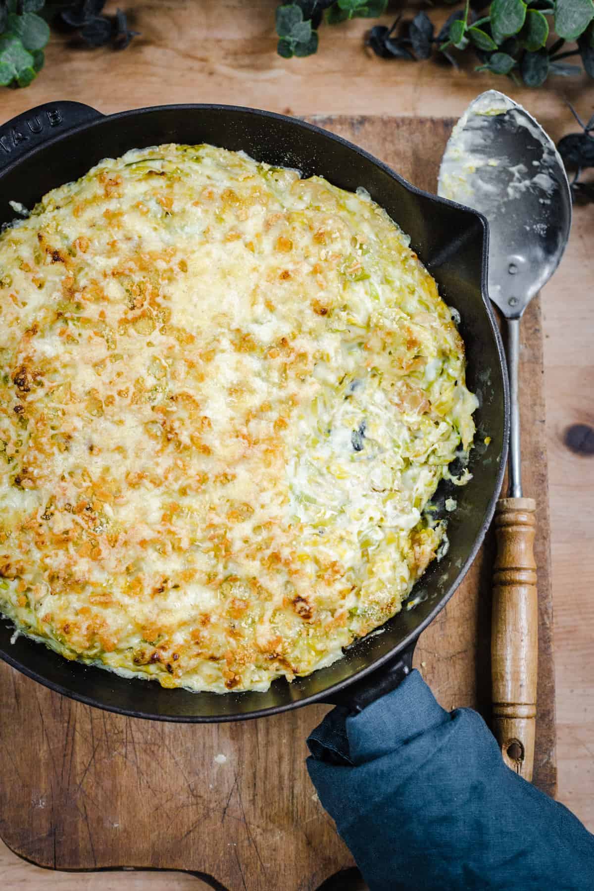 Overhead close shot of Cheesy & Creamy Brussels Sprouts Gratin in a cast iron pan on top of a wooden board.