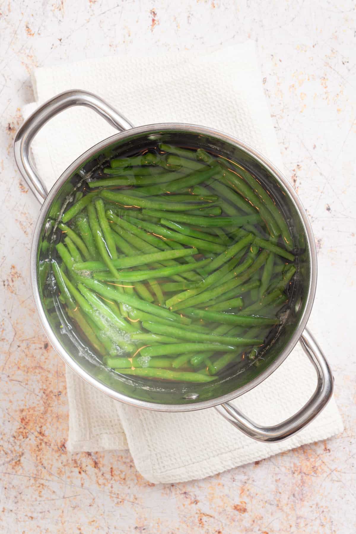 An overhead image of green beans being simmered in water in a large pot.
