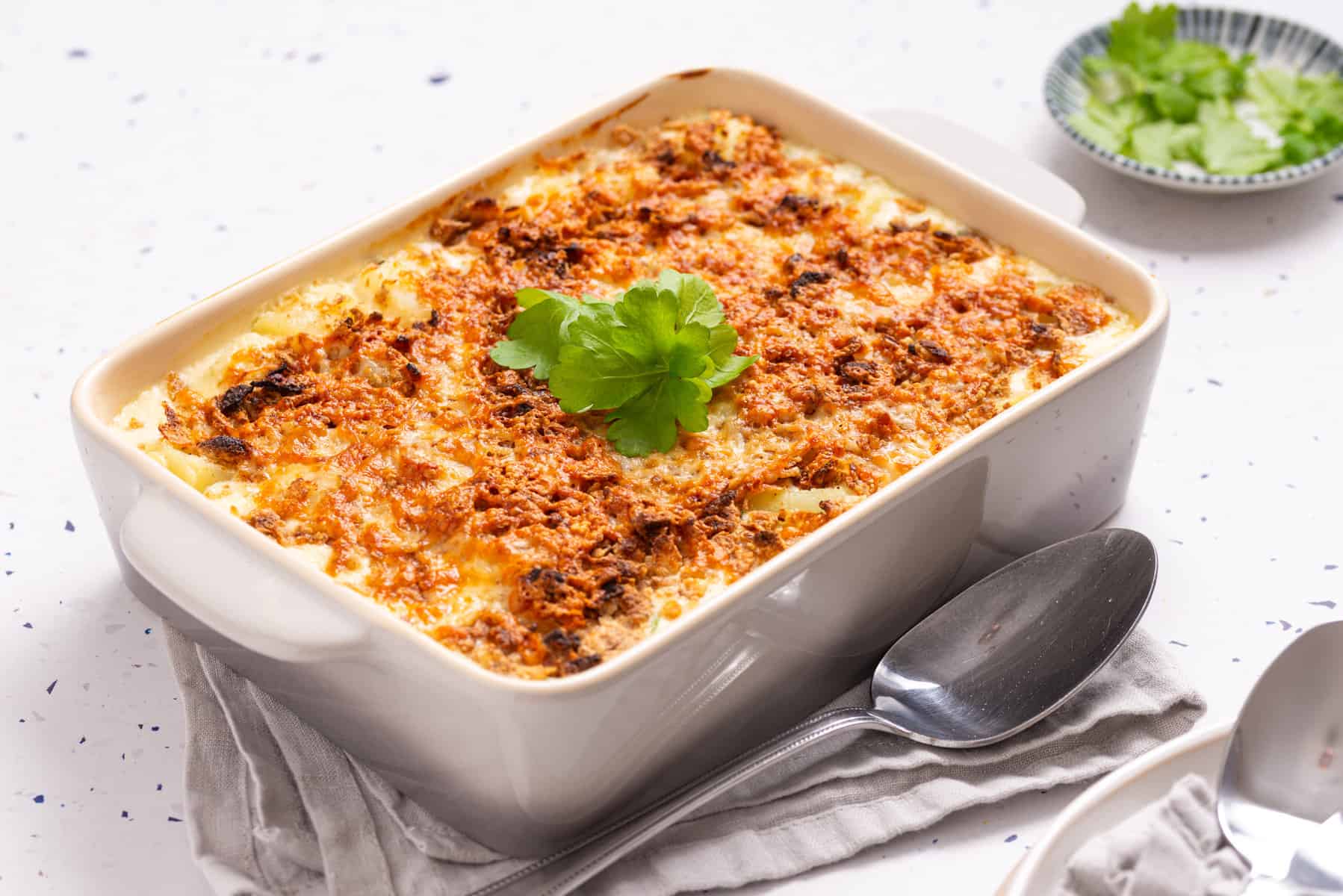 A close up image of cheesy potatoes in a casserole, garnished with parsley.