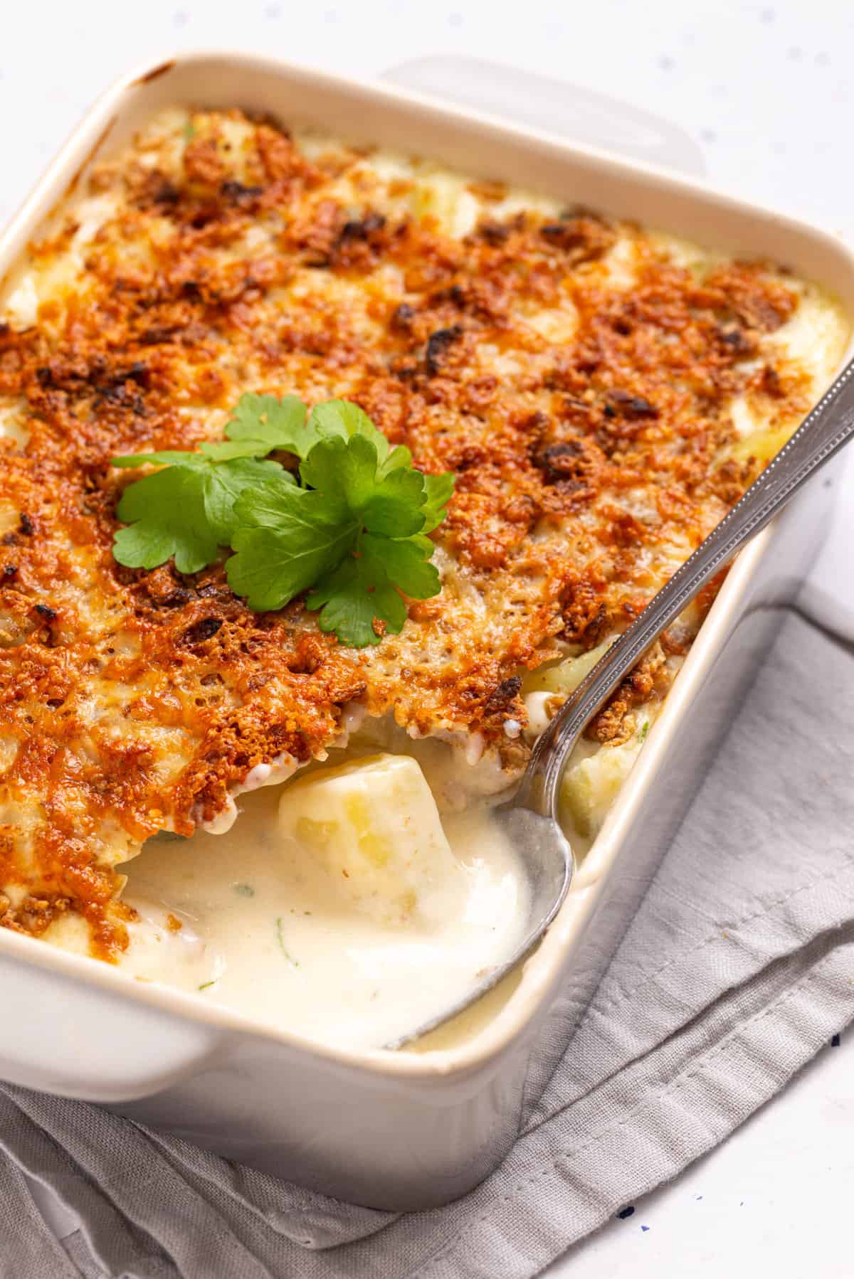 A close up image of baked cheesy potatoes with a serving of it missing and a spoon resting on the missing portion.