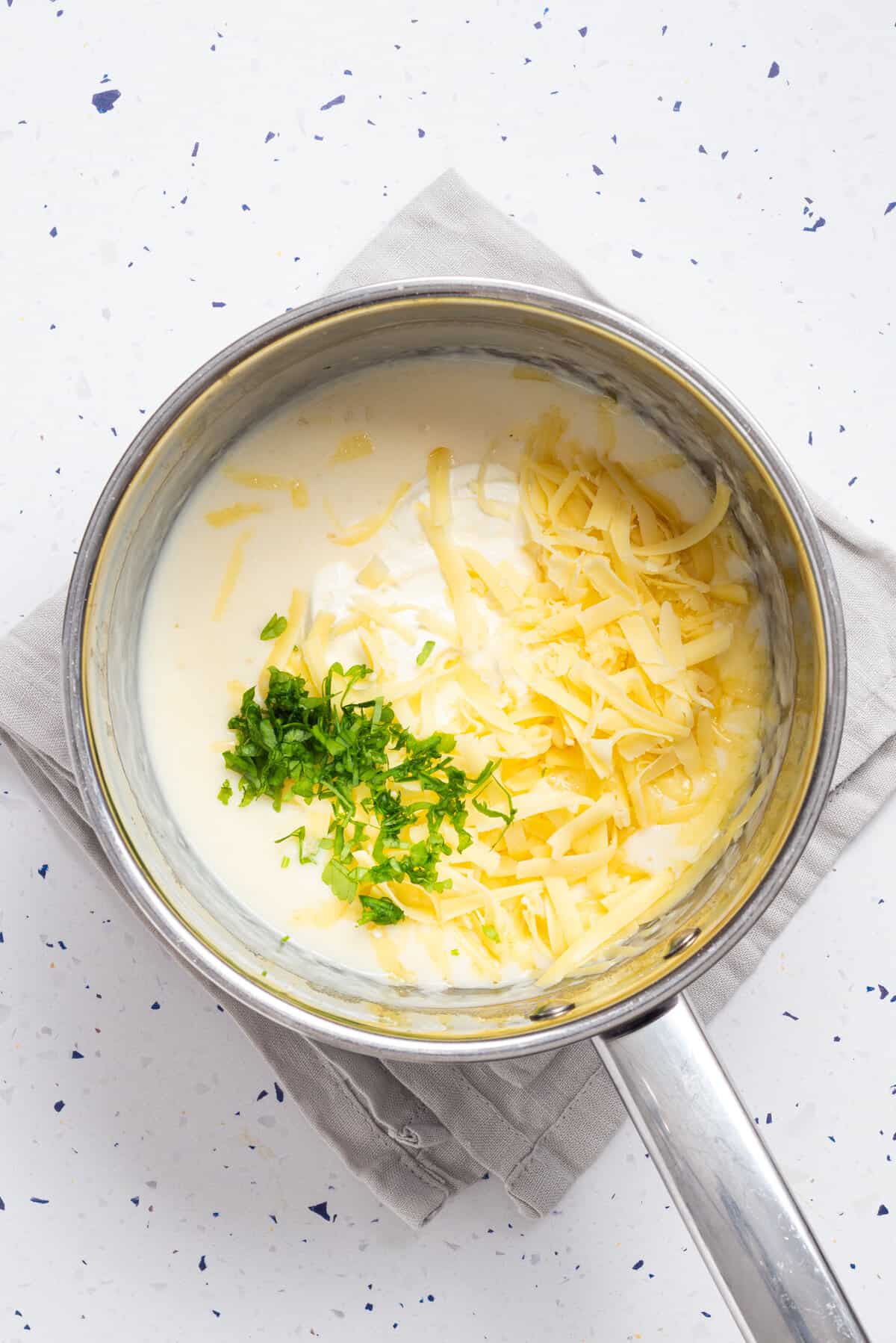 An overhead image of sour cream, parsley, salt and cheese added to a pot.