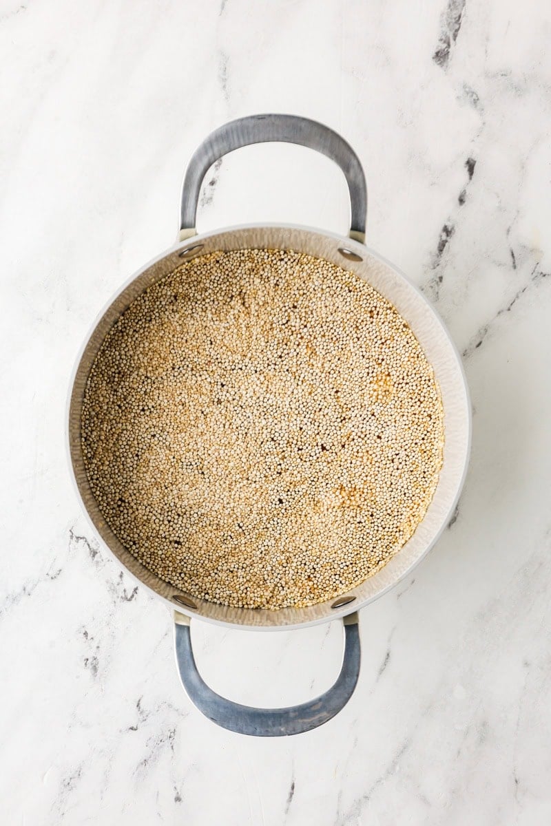 An overhead image of quinoa and vegetable broth in a medium saucepan.