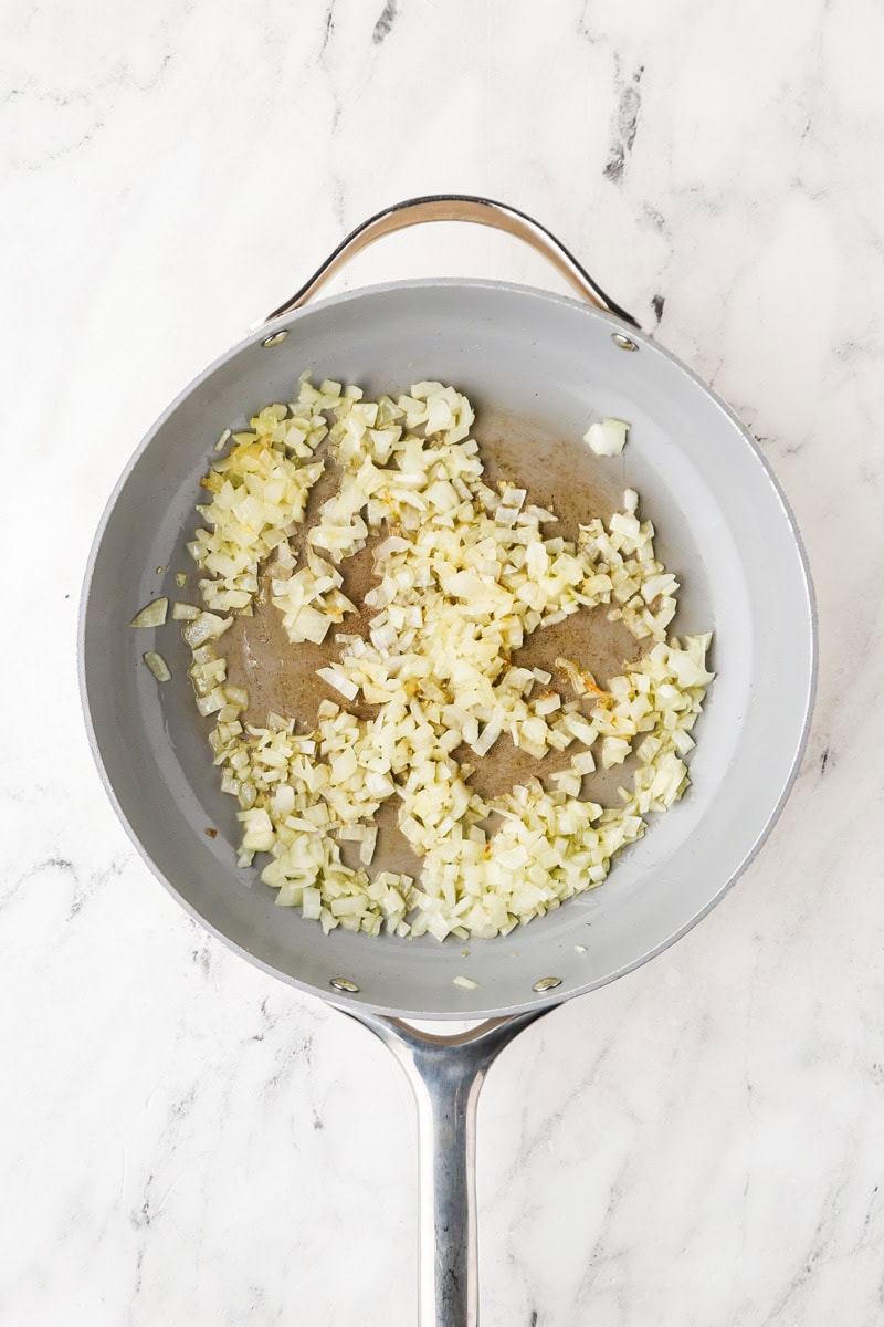 An overhead image of sauteing garlic, onions, ginger, and chili in a skillet.