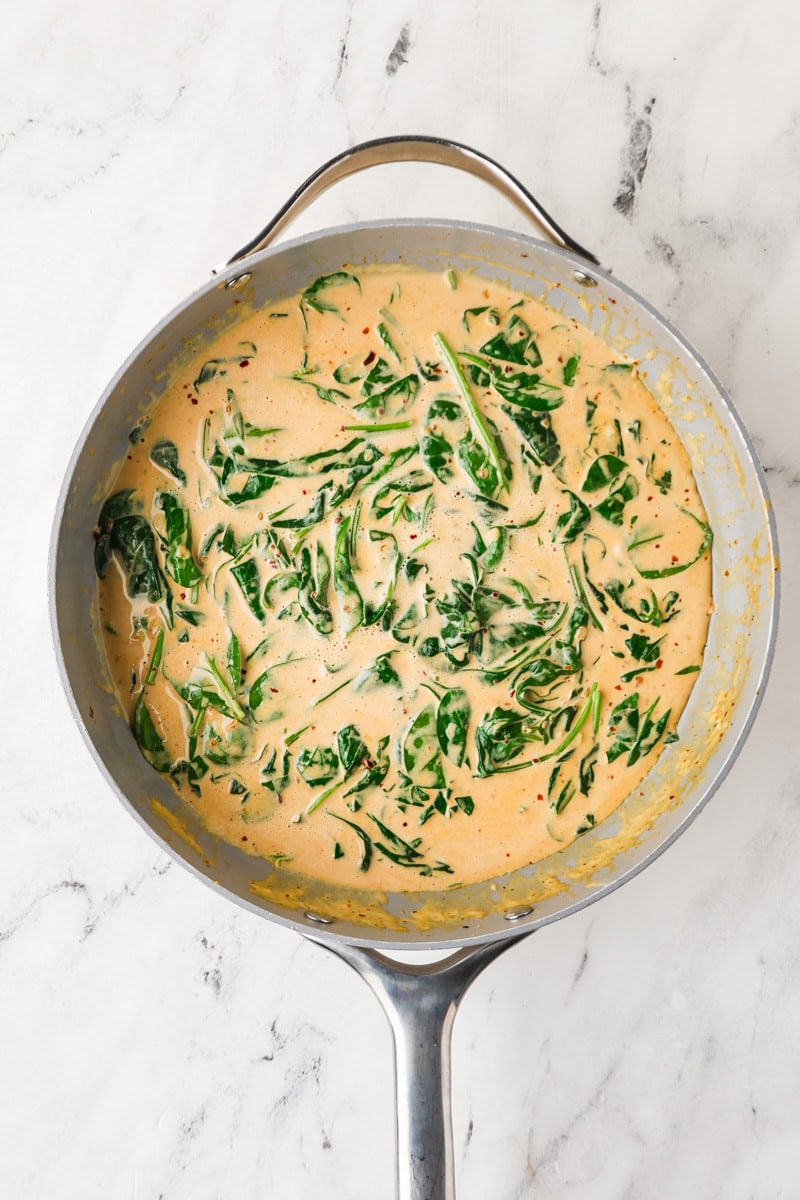 An overhead image of adding the baby spinach to the sauce.