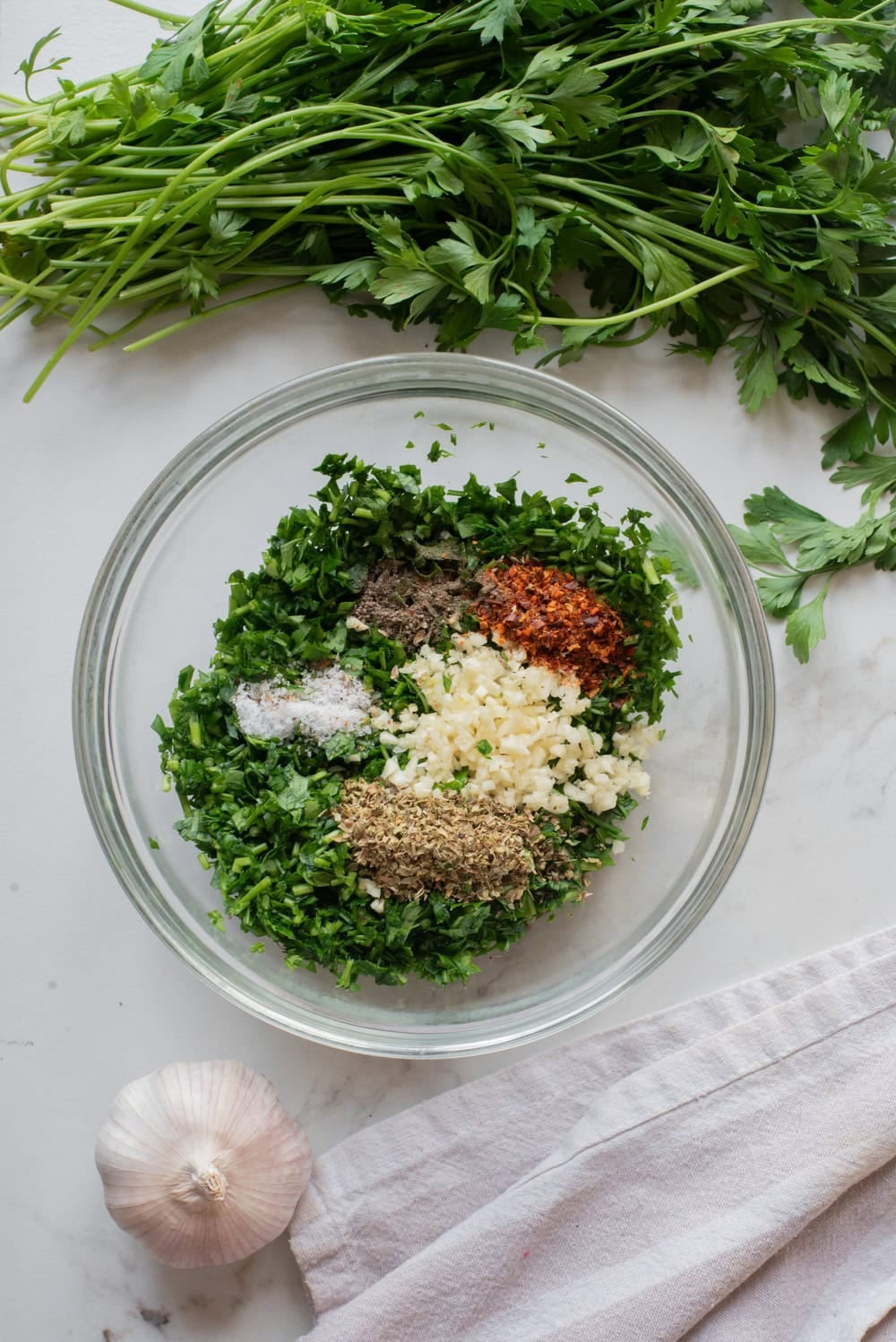 Chopped parsley mixed with garlic, oregano, red pepper flakes, salt, and black pepper in a bowl.
