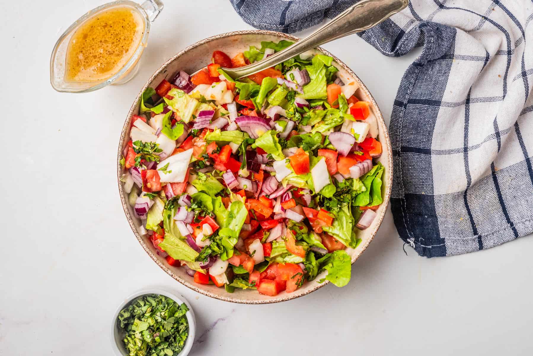 An overhead image of vegan chopped salad in a bowl with a serving spoon in the middle.