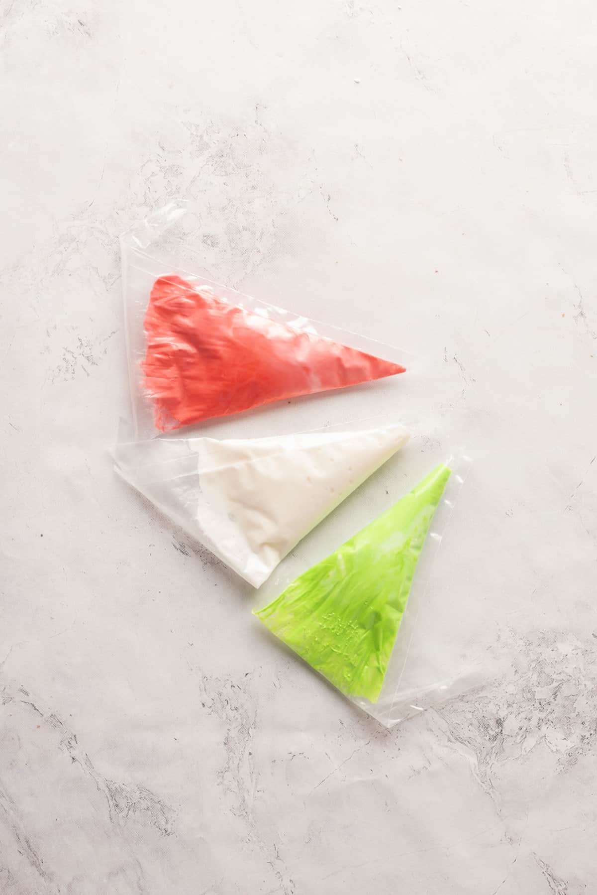 Overhead view showing three bags of icing mixture in red, white and green colors.