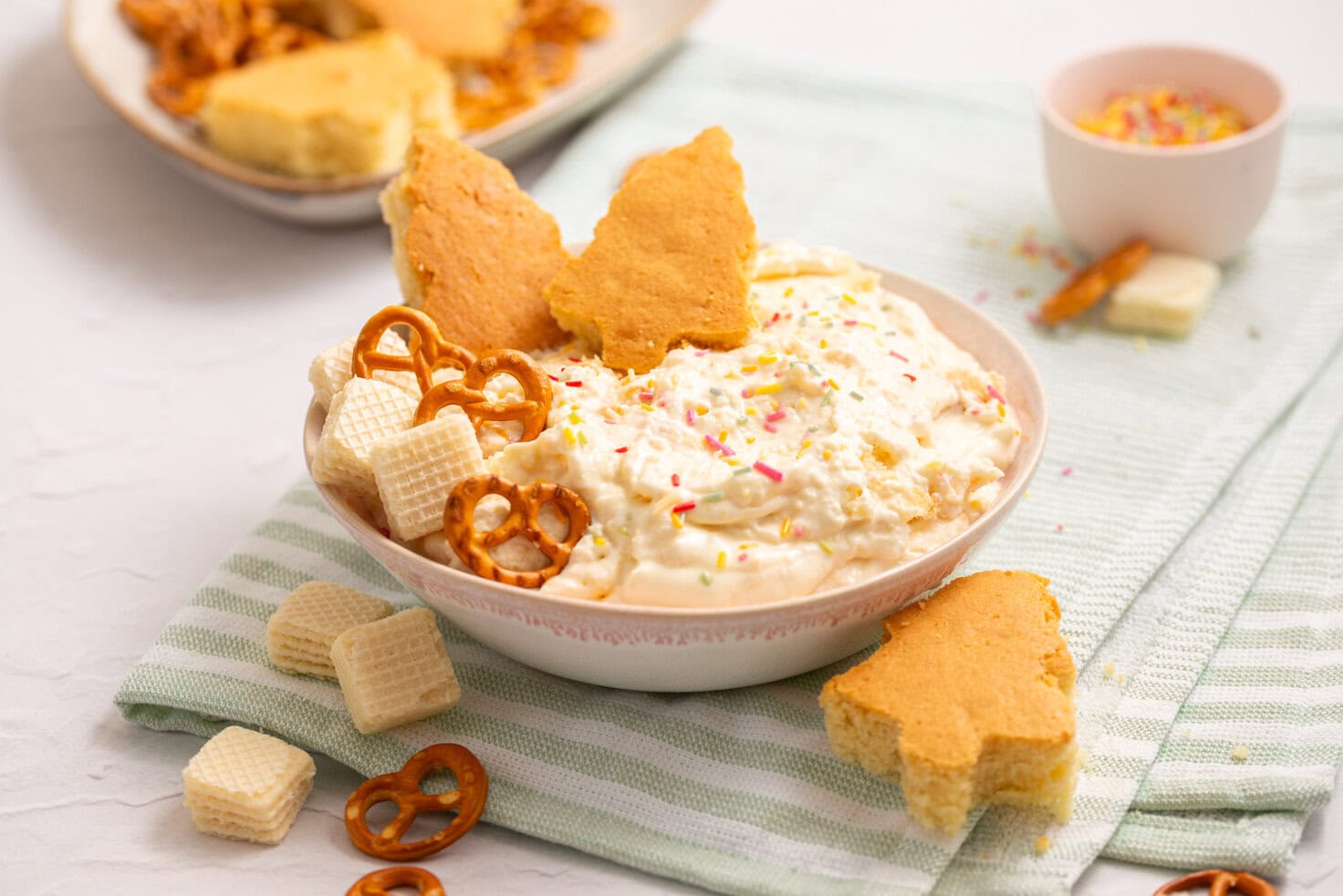 Homemade Christmas Tree Cake Dip served with tree-shaped vanilla cake pieces, pretzels, and vanilla wafers.