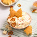Bowl of homemade Christmas Tree Cake Dip topped with sprinkles and served with homemade tree-shaped cake pieces, pretzels, and vanilla wafers.