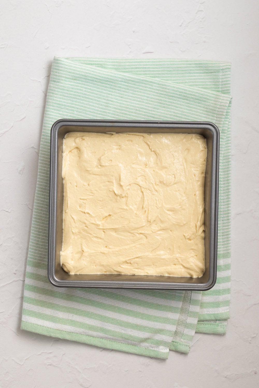 Vanilla-almond cake batter spread evenly into an 8-inch square baking pan before baking.