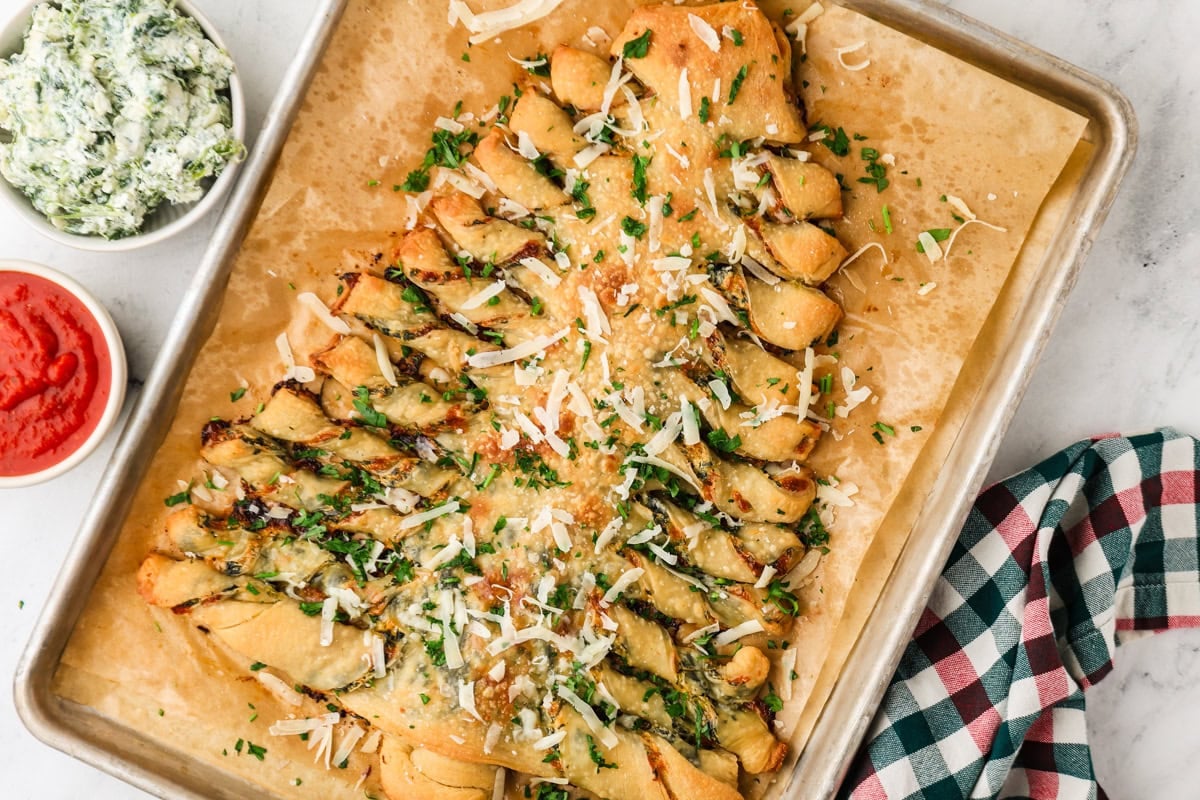 Christmas tree spinach dip breadsticks served with spinach dip and marinara on a baking sheet.