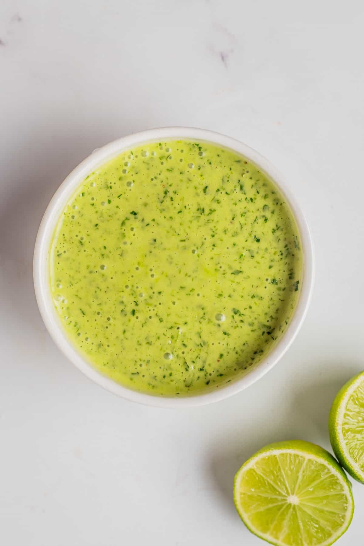 An overhead image of finished cilantro lime dressing in a small bowl with sliced limes on the side.