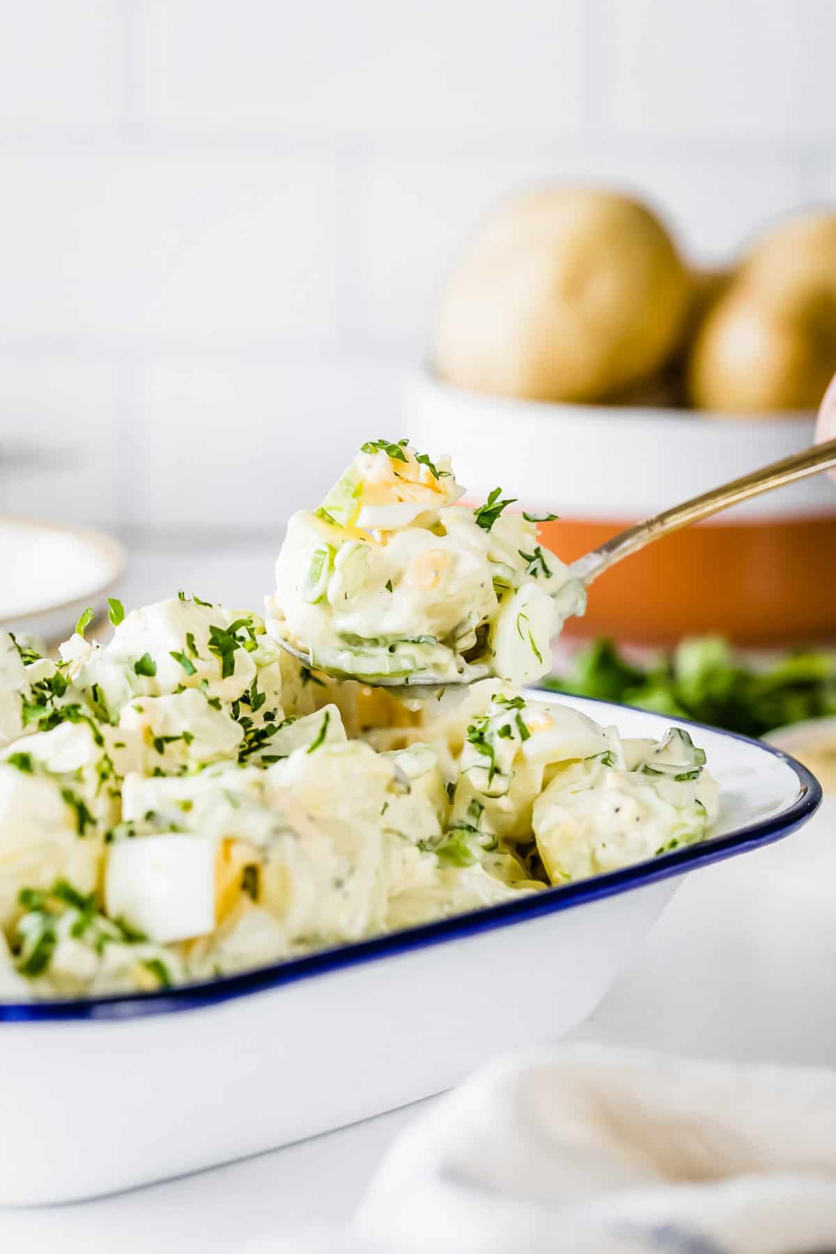 Spoonful of potato salad being lifted from the baking dish with the rest of the potato salad.