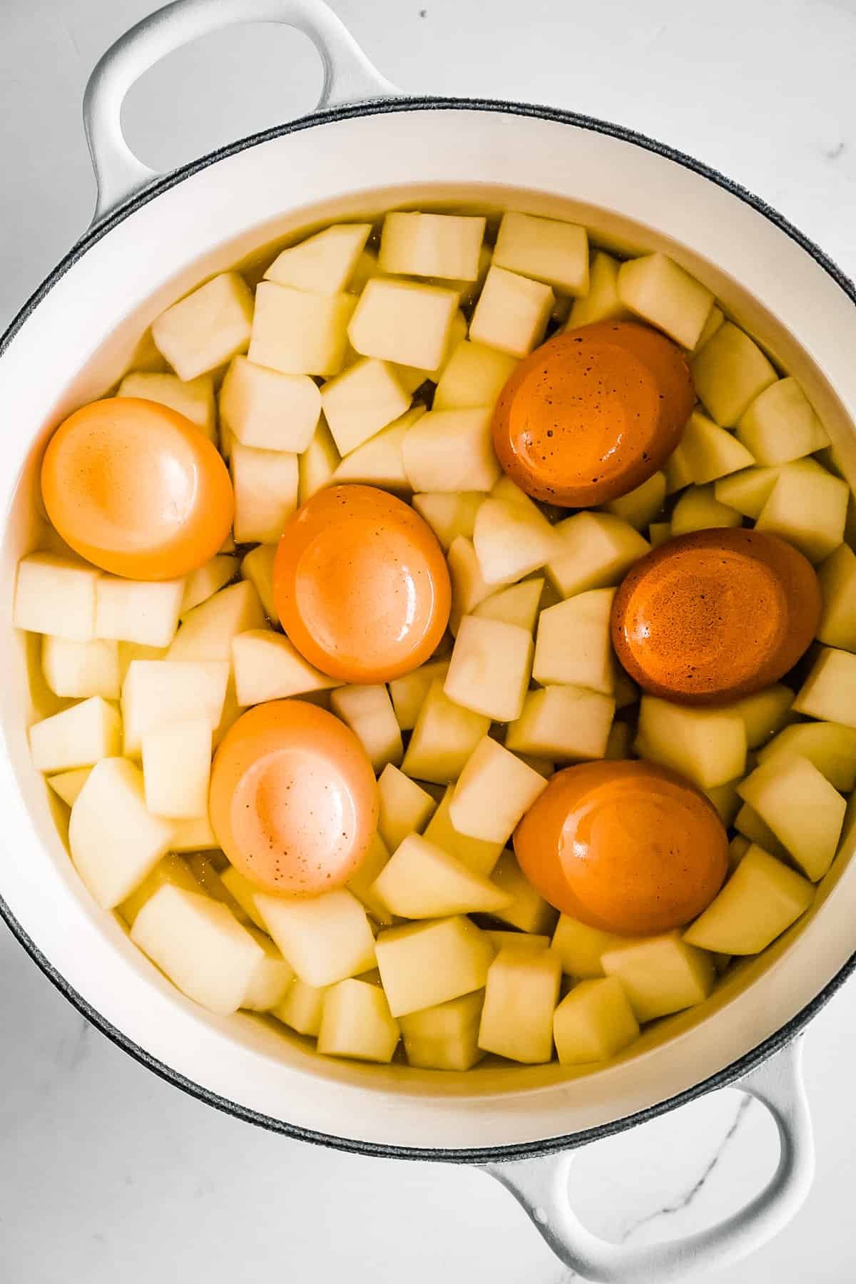 Overhead view of quartered potatoes and eggs in a large Dutch oven.