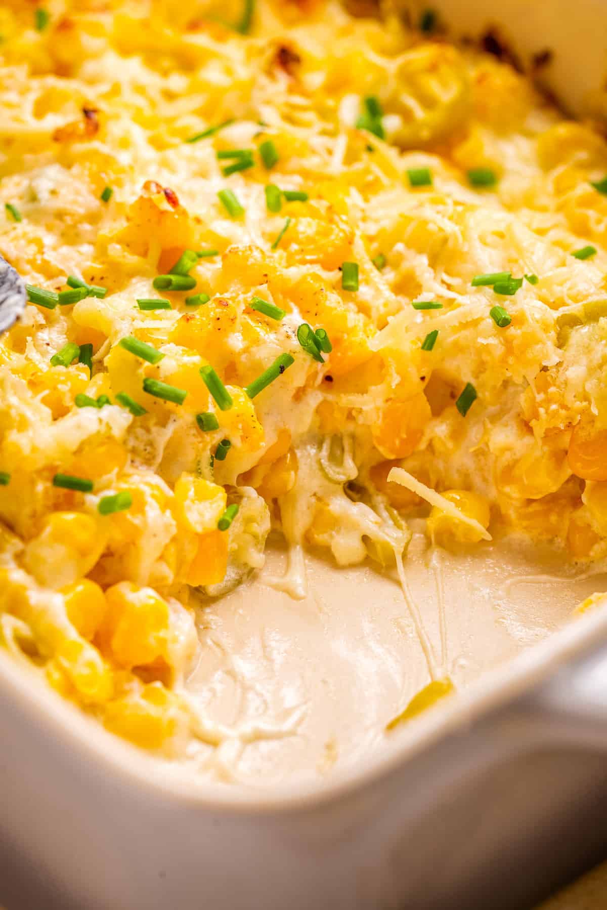 A close up image of corn casserole with cream cheese, with a portion taken out