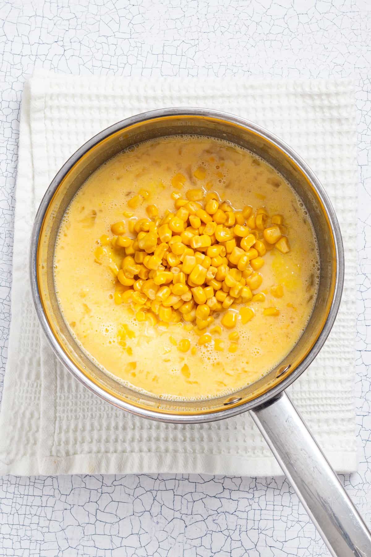An overhead image of sugar, milk,, creamed corn and whole kernel corns cooked together in a saucepan.