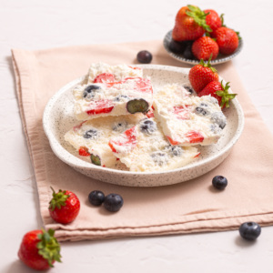 Several squares of berry cottage cheese bark served on a plate with fresh strawberries and blueberries.