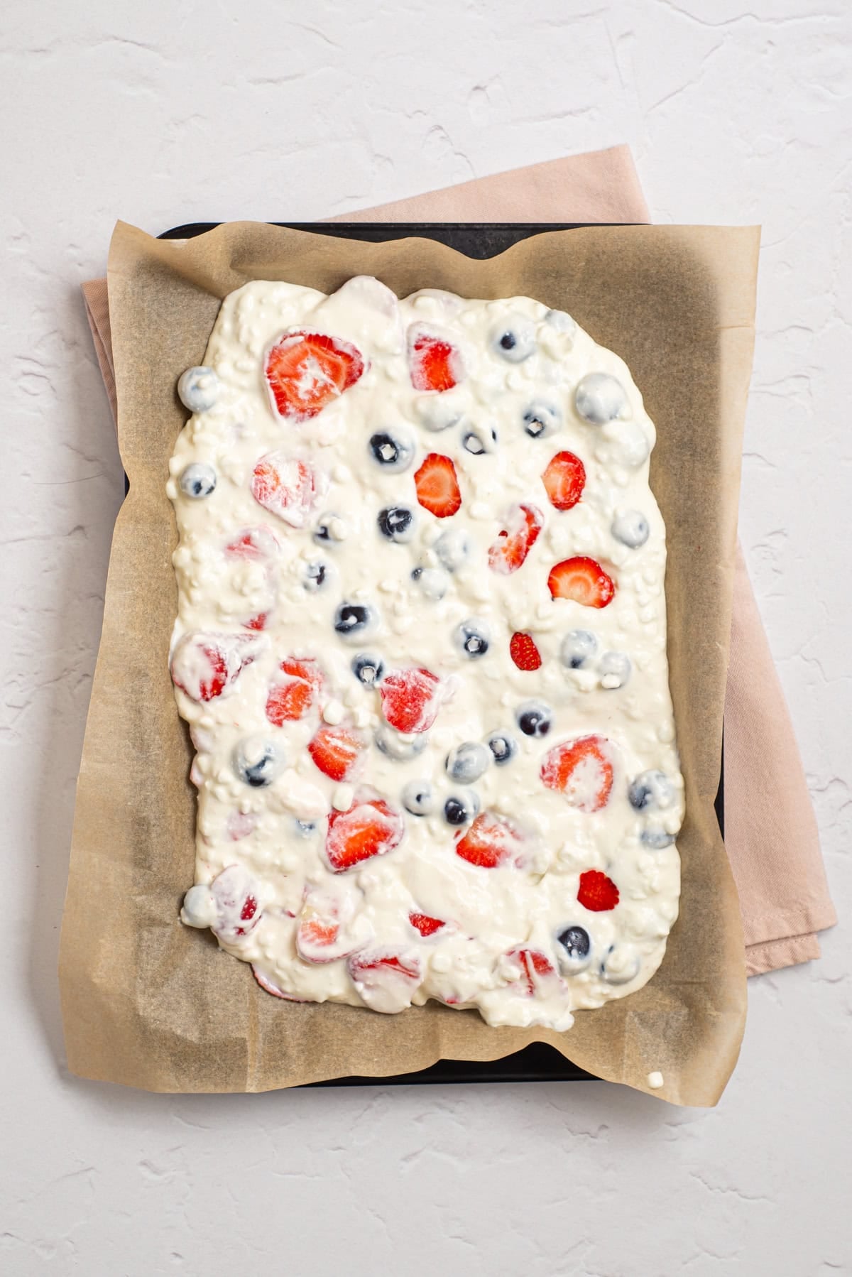 Cottage cheese bark mixture spread onto parchment paper and topped with berries and coconut.