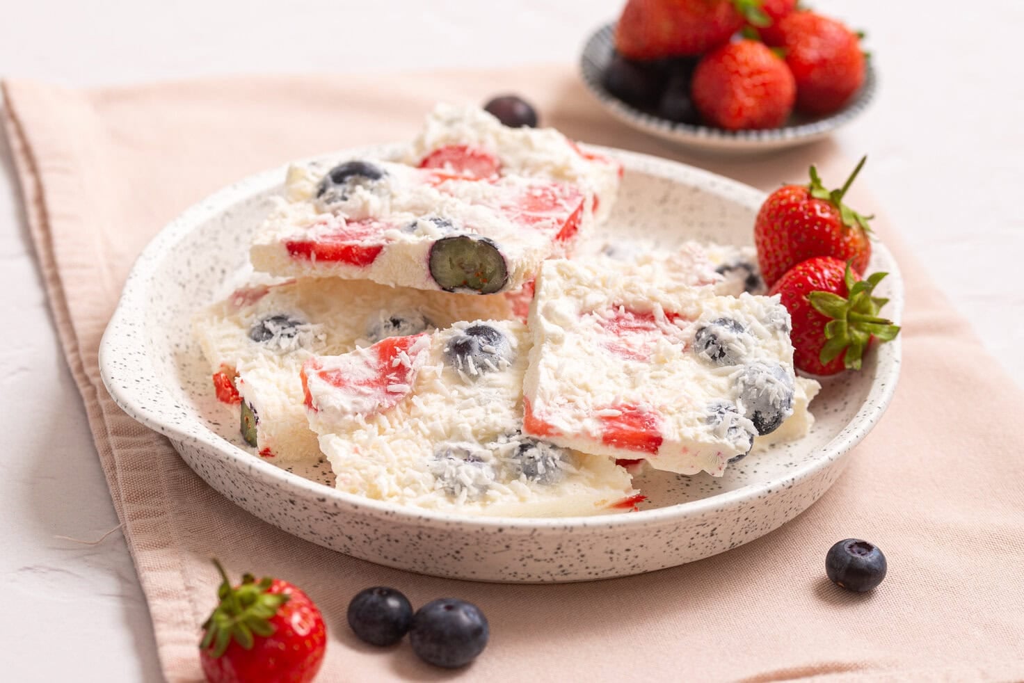 Plate of frozen cottage cheese bark pieces served with fresh strawberries and blueberries.