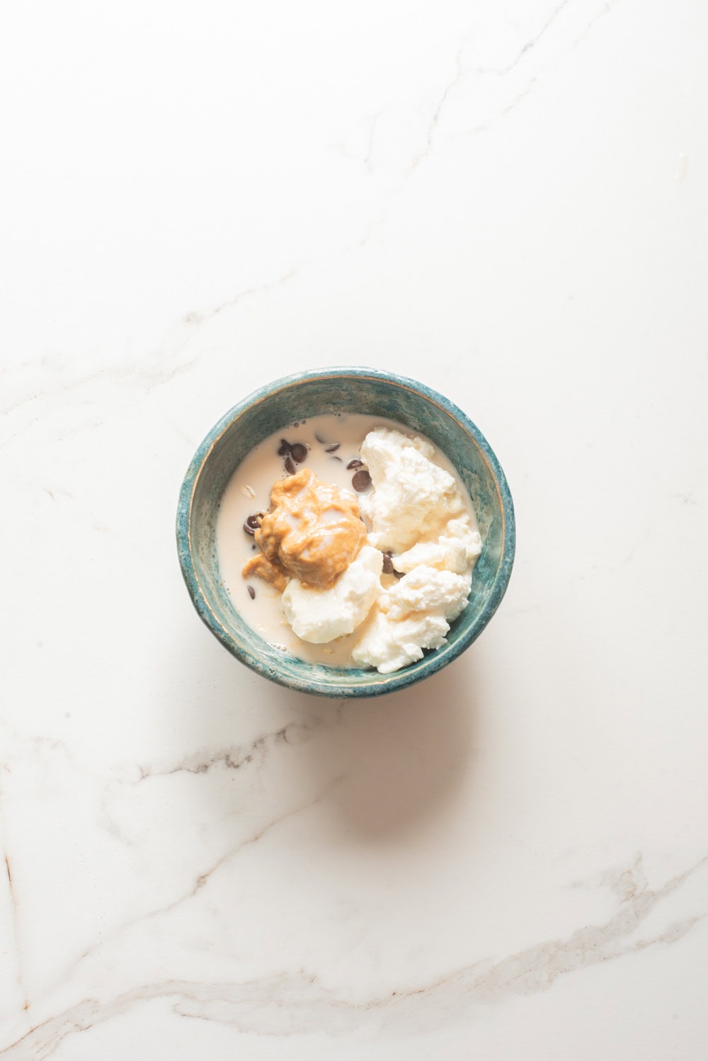 Overhead image of the ingredients of cottage cheese cookie dough overnight oats ingredients before mixing in a bowl.