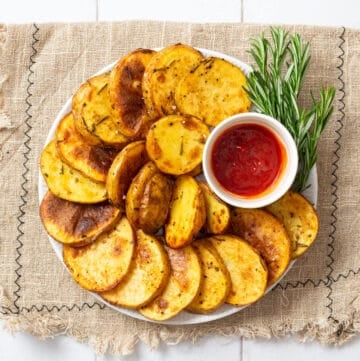 An overhead image of cottage fries arranged on a plate with ketchup in a small bowl and rosemary on the side.