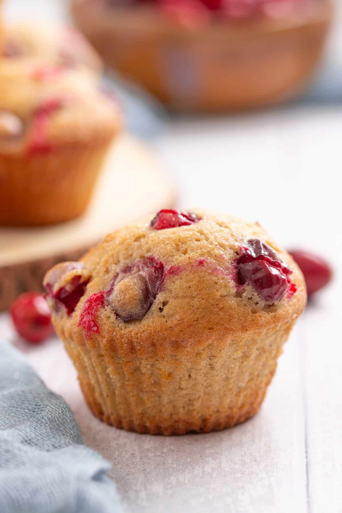 A close up image of a single cranberry orange muffin on a table.