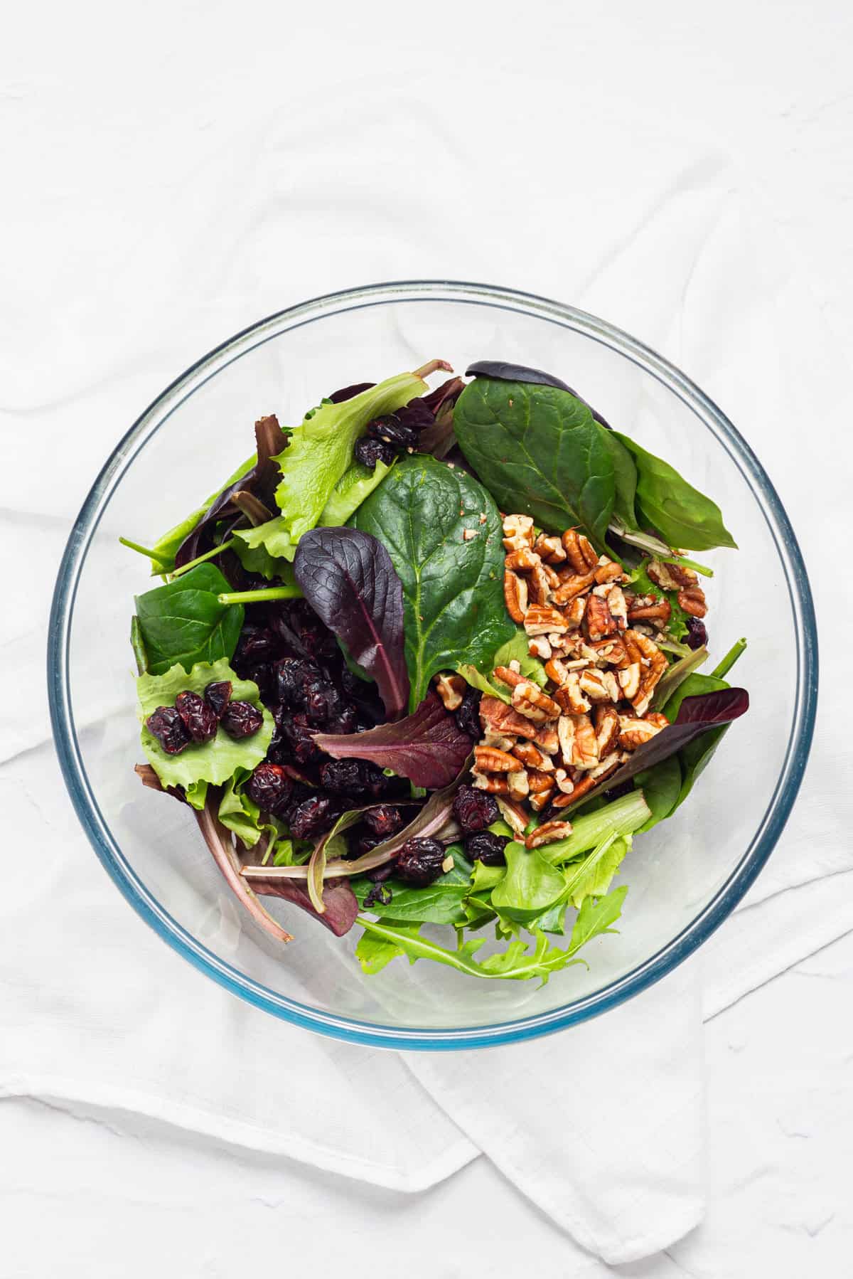 An overhead image of mixed salad greens, cranberries, and pecans.