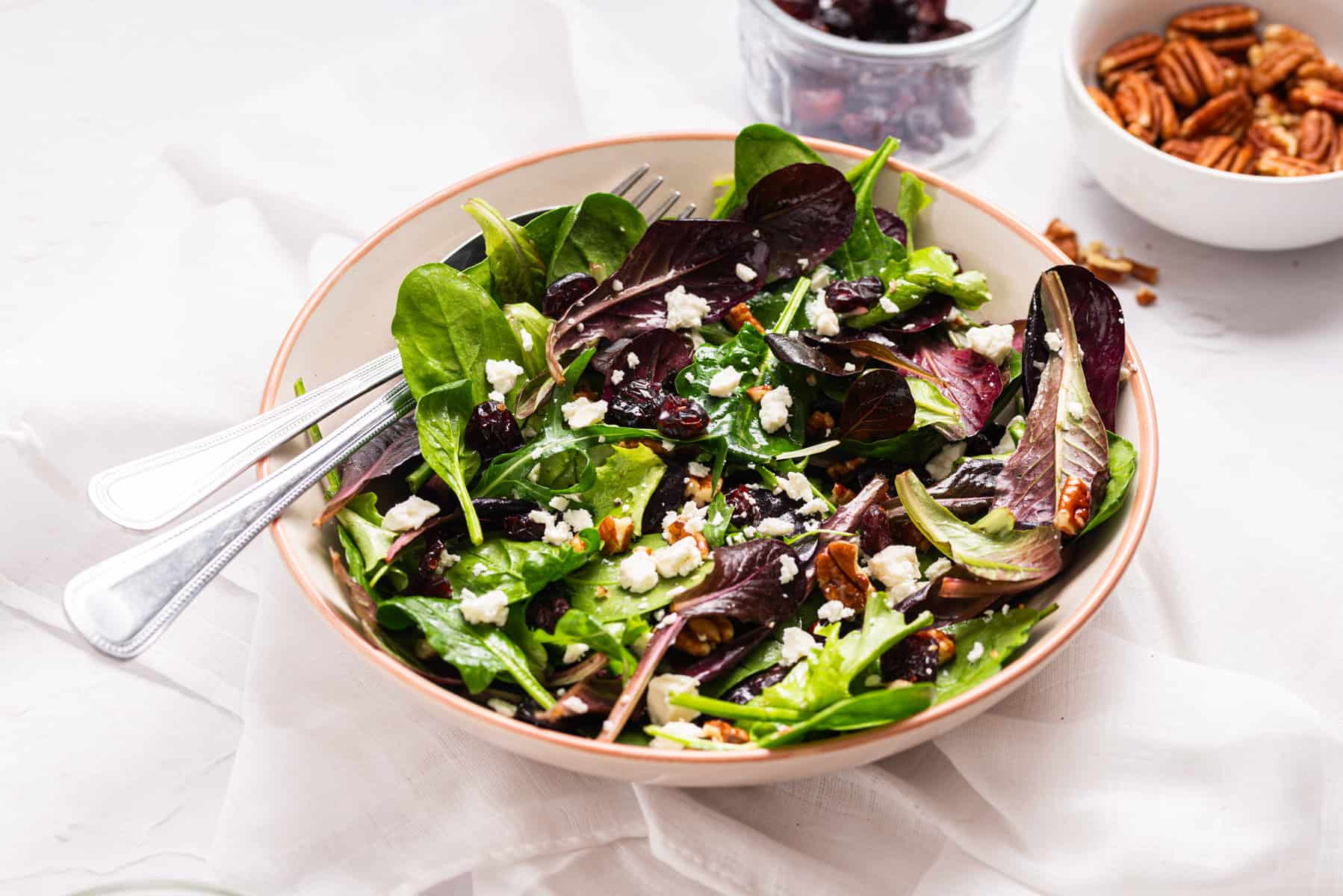 An image of cranberry salad with pecans served in a white salad bowl with a fork on the side.