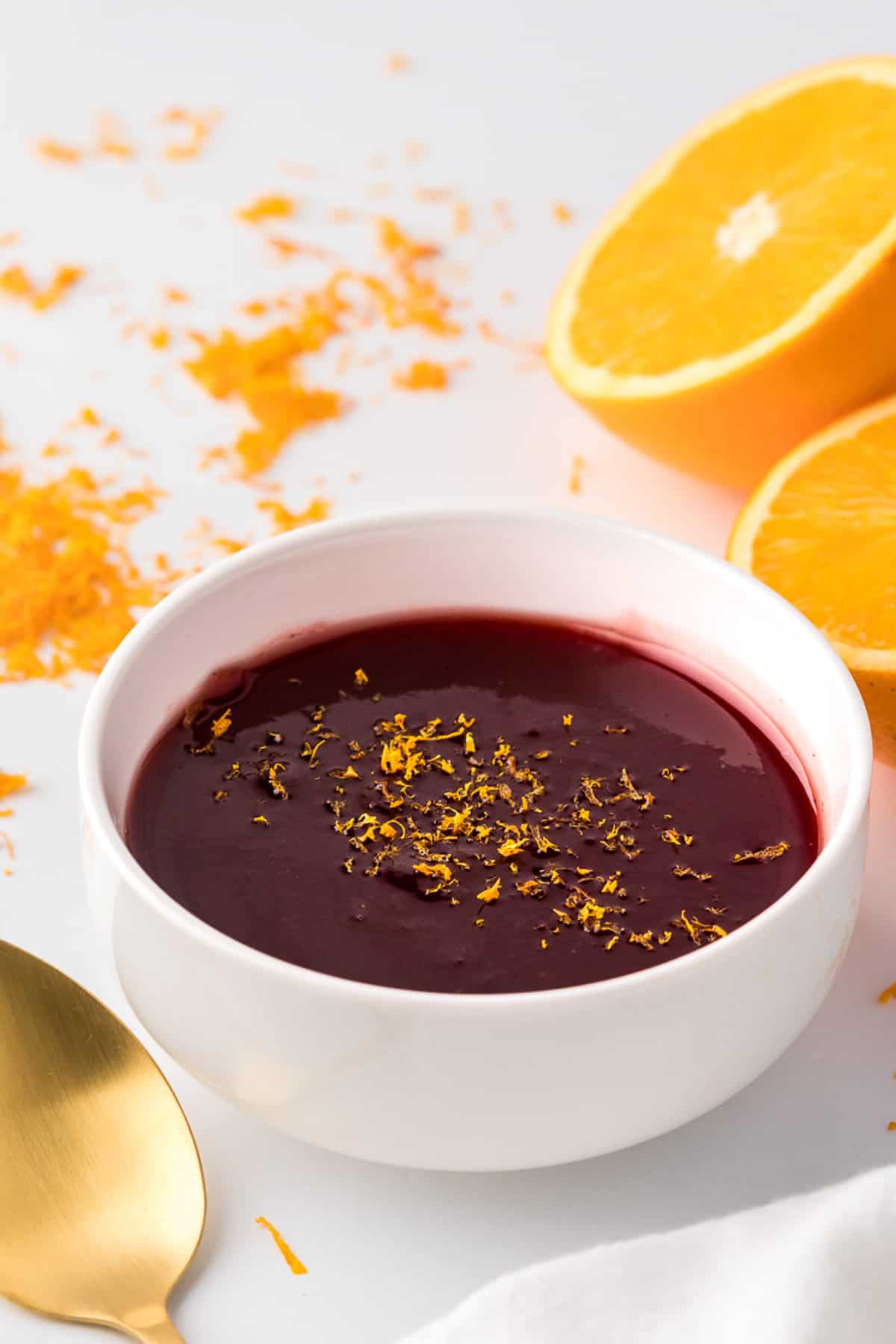 Close up view of cranberry sauce in white bowl, with oranges in the background.