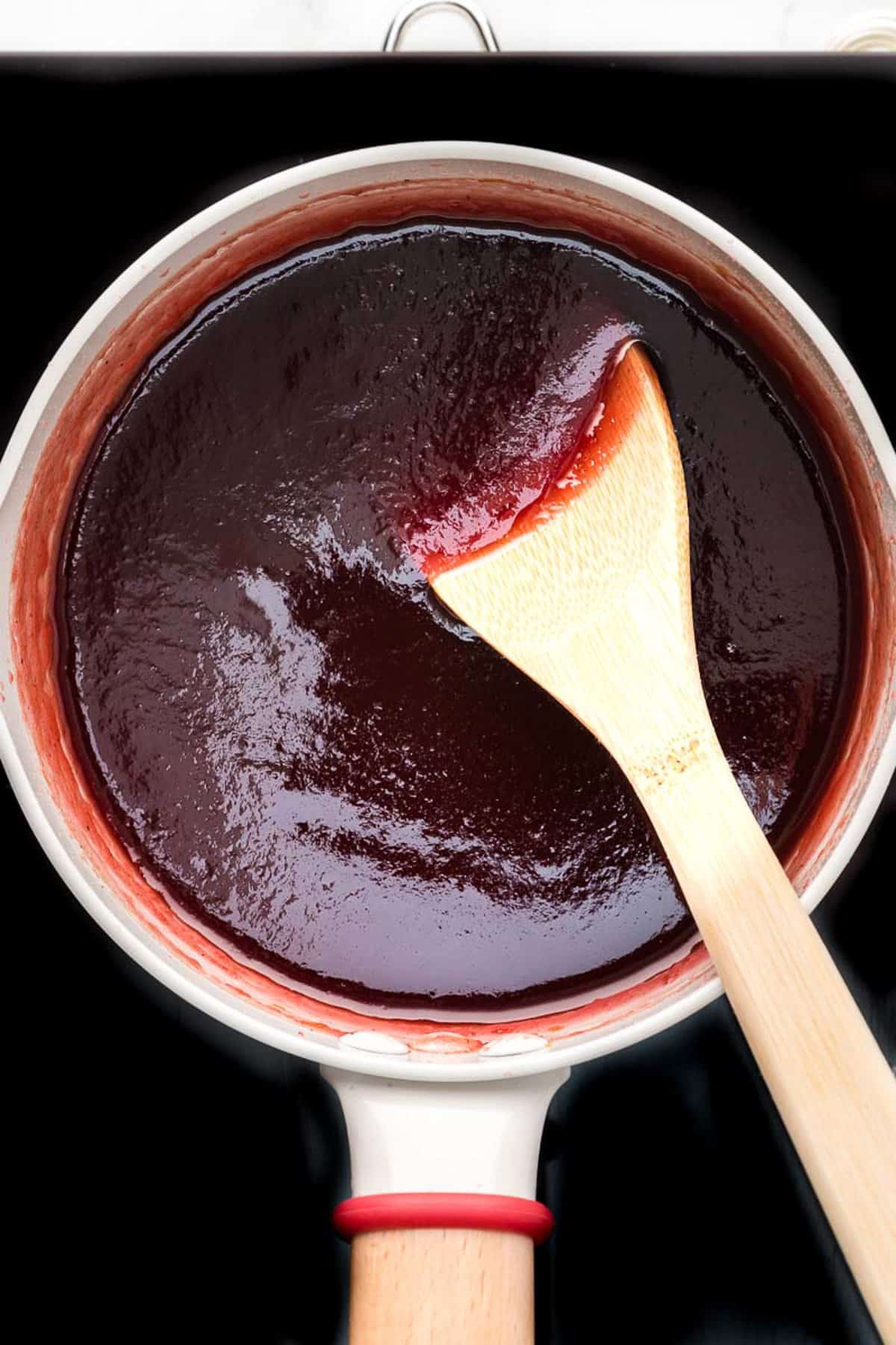 Overhead view showing smooth cranberry sauce with wooden spatula in the pot.