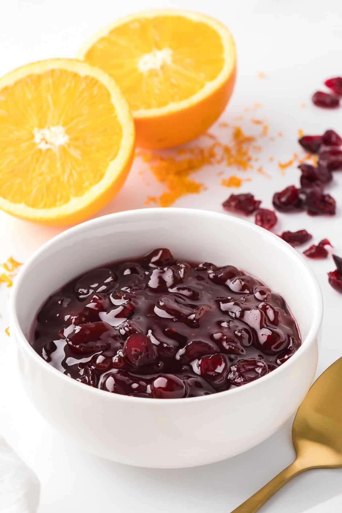 Close up view of cranberry sauce in white bowl with oranges in the background