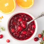 Overhead view of cranberry sauce in white ramekin with orange slices in the background.
