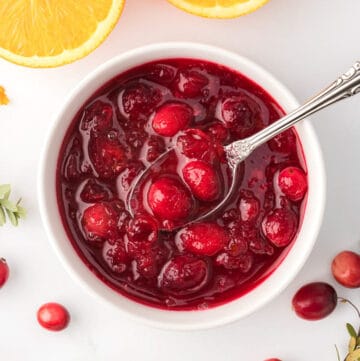 Close up shot of cranberry sauce in white ramekin with a spoon in it.