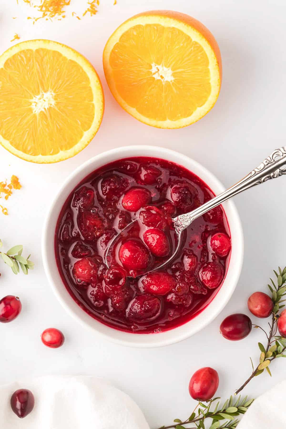 Overhead view of cranberry sauce in white ramekin with orange slices in the background.