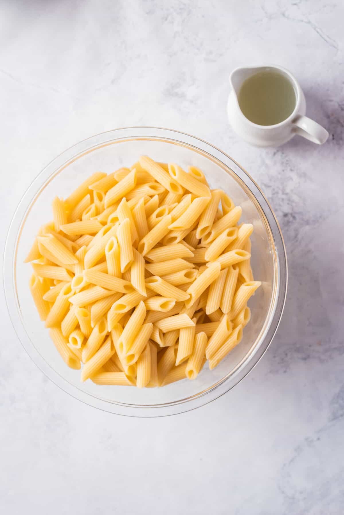 Overhead view of a transparent bowl with drained pasta next to the reserved pasta water placed in a container.