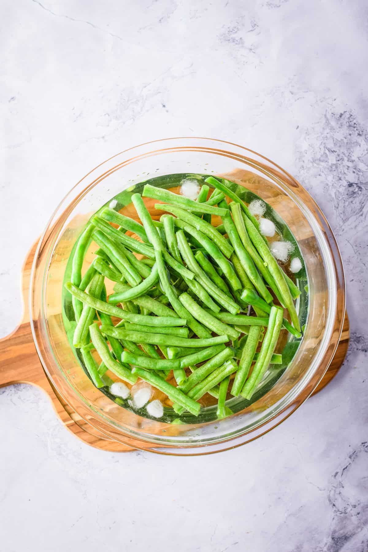 Overhead view of green beans in ice cold water in glass bowl.